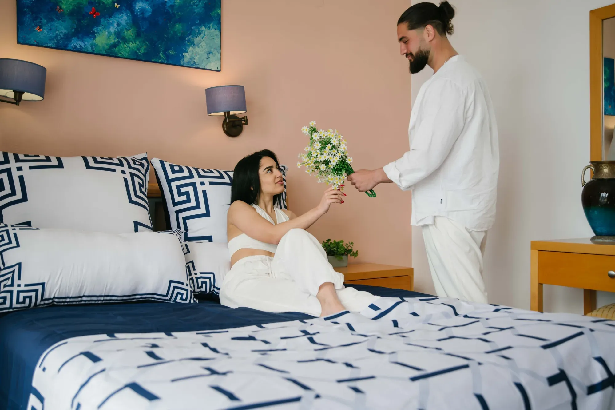 A man hands flowers to a woman sitting on a bed made in Ionian Harmony