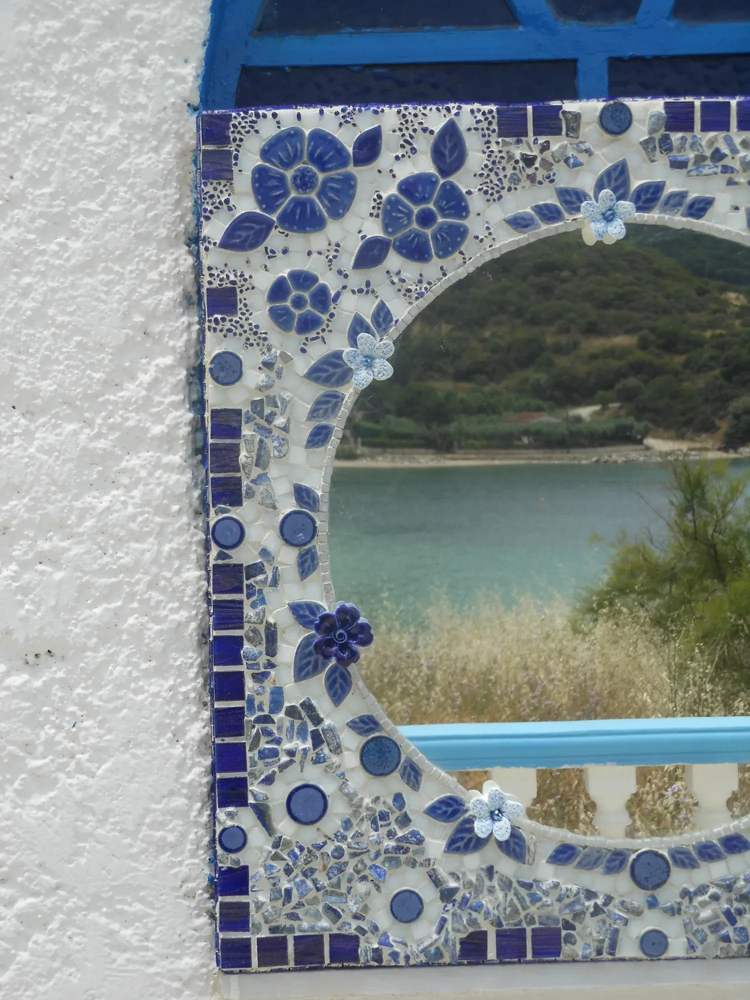 The tall floral mirror reflecting a bay and a green hillside